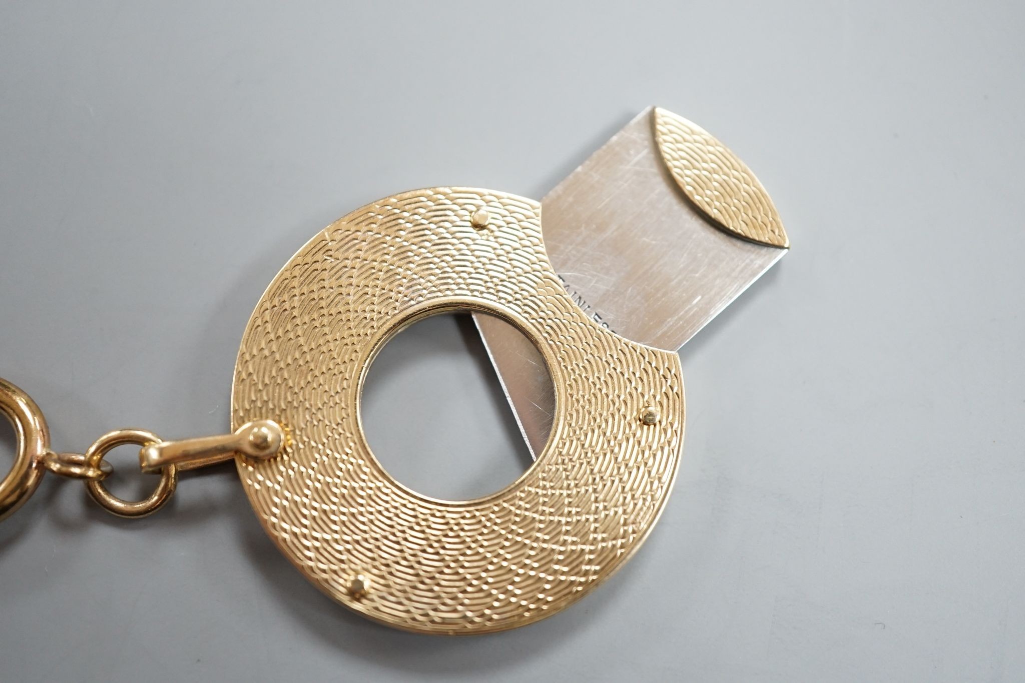 A 1960's engine turned 9ct gold mounted circular cigar cutter, 34mm, with gilt metal fob clip.